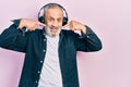 Handsome senior man with beard listening to music using headphones smiling cheerful showing and pointing with fingers teeth and Royalty Free Stock Photo