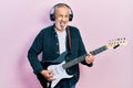 Handsome senior man with beard playing electric guitar sticking tongue out happy with funny expression Royalty Free Stock Photo