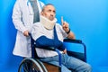 Handsome senior man with beard sitting on wheelchair with neck collar pointing up looking sad and upset, indicating direction with Royalty Free Stock Photo