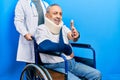 Handsome senior man with beard sitting on wheelchair with neck collar smiling friendly offering handshake as greeting and Royalty Free Stock Photo