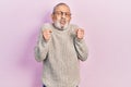 Handsome senior man with beard wearing casual sweater and glasses excited for success with arms raised and eyes closed celebrating Royalty Free Stock Photo