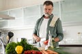 Handsome senior man cooking at home preparing salad in kitchen Royalty Free Stock Photo