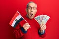 Handsome senior man with grey hair holding egypt flag and egyptian pounds banknotes afraid and shocked with surprise and amazed Royalty Free Stock Photo