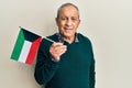 Handsome senior man with grey hair holding kuwait flag looking positive and happy standing and smiling with a confident smile