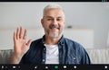 Handsome senior man having video conference, waving at camera