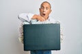 Handsome senior man holding briefcase full of dollars in shock face, looking skeptical and sarcastic, surprised with open mouth Royalty Free Stock Photo