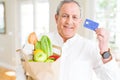 Handsome senior man holding paper bag full of fresh groceries and showing credit card as payment Royalty Free Stock Photo