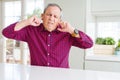 Handsome senior man at home covering ears with fingers with annoyed expression for the noise of loud music