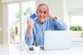 Handsome senior man shopping online using credit card and laptop at home with happy face smiling doing ok sign with hand on eye Royalty Free Stock Photo