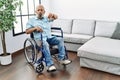 Handsome senior man sitting on wheelchair at the living room looking unhappy and angry showing rejection and negative with thumbs Royalty Free Stock Photo