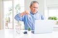 Handsome senior man using computer laptop working on internet with angry face, negative sign showing dislike with thumbs down,