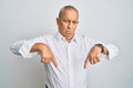 Handsome senior man wearing casual white shirt pointing down looking sad and upset, indicating direction with fingers, unhappy and Royalty Free Stock Photo