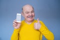 Handsome senior man in yellow sweater shows thumb up and phone screen Royalty Free Stock Photo