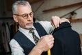 handsome senior tailor measuring jacket with tape measure