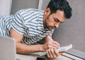 Handsome serious Caucasian male student learning lessons lying on the carpet t home with textbooks, making notes. Young business Royalty Free Stock Photo