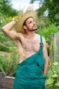 Handsome gardener with green pants and straw hat standing in garden