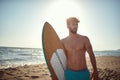 Handsome sexy young  man standing on the sunny beach, holding surfboard Royalty Free Stock Photo