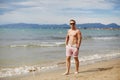 Handsome shirtless athletic young guy walking on the beach by the waterline. Young muscular man with perfect body in Royalty Free Stock Photo