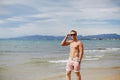 Handsome shirtless athletic young guy walking on the beach by the waterline. Young muscular man with perfect body in Royalty Free Stock Photo