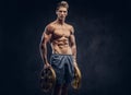 Handsome shirtless ectomorph bodybuilder with stylish hair posing with a barbell disk on dark background.