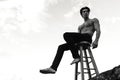 Handsome shirtless muscular young man posing outdoor, seated on chair. Photo white and black Royalty Free Stock Photo