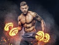 Handsome shirtless tattooed bodybuilder with stylish haircut and beard, wearing sports shorts, posing in a studio. Fire