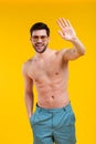 handsome shirtless young man in shorts and sunglasses waving hand and smiling at camera Royalty Free Stock Photo