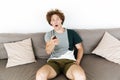 Handsome shocked man sitting on sofa holding remote control