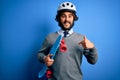 Handsome skater man with beard wearing security helmet holding skate over blue background with surprise face pointing finger to Royalty Free Stock Photo