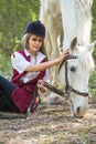 Handsome woman sitting on the ground with brown horse near her. Royalty Free Stock Photo