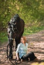 Handsome woman sitting on the ground with brown horse near her. Royalty Free Stock Photo