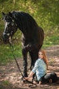 Handsome woman sitting on the ground with brown horse near her. Royalty Free Stock Photo