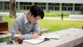 A handsome and smart Asian college man is focusing on reading a book in the campus park Royalty Free Stock Photo