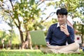 Handsome Asian male college student using laptop, sipping coffee, while sitting in the campus`s park Royalty Free Stock Photo