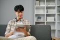A handsome Asian man using his digital tablet, focuses on his work on tablet while sitting on a sofa Royalty Free Stock Photo