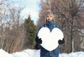 Handsome smiling bearded hipster man holding a big heart made of snow, standing on snowy road in winter park. Fall in love. Royalty Free Stock Photo