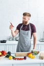 handsome smiling bearded man in apron listening music in earphones and holding chili pepper while cooking Royalty Free Stock Photo
