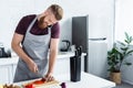 handsome smiling bearded man in apron talking by smartphone and cutting vegetables in kitchen Royalty Free Stock Photo