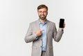 Handsome smiling businessman with beard, wearing grey suit and glasses, pointing finger at mobile phone screen, showing Royalty Free Stock Photo