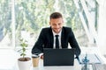 Handsome smiling businessman in elegant suit working on laptop in a bright modern office Royalty Free Stock Photo