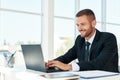 Handsome smiling businessman in elegant suit working on laptop in a bright modern office Royalty Free Stock Photo