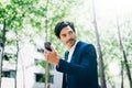 Handsome smiling businessman using smartphone for listining music while walking in city park.Horizontal,blurred Royalty Free Stock Photo