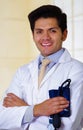 Handsome smiling doctor posing and looking at camera with a tensiometer in his hands with crossed arms, in office