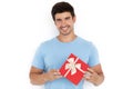 Handsome smiling European man in blue t-shirt holding red gift box against white wall Royalty Free Stock Photo