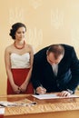 Handsome smiling groom in stylish suit signing marriage contract during wedding ceremony in registry office, newlywed family Royalty Free Stock Photo