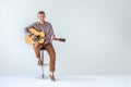 Handsome smiling guitarist play music siting on chair