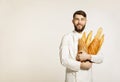 Handsome smiling happy baker in uniform holding baguettes with b