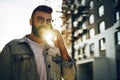Handsome hipster businessman with beard, in denim jacket and trendy glasses walks around city and calls on mobile phone Royalty Free Stock Photo