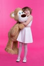 Handsome smiling little girl hugging a toy bear on an isolated pink background Royalty Free Stock Photo