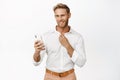Handsome smiling macho man holding mobile phone, adjusting his shirt and looking self-assured and flirty at camera Royalty Free Stock Photo
